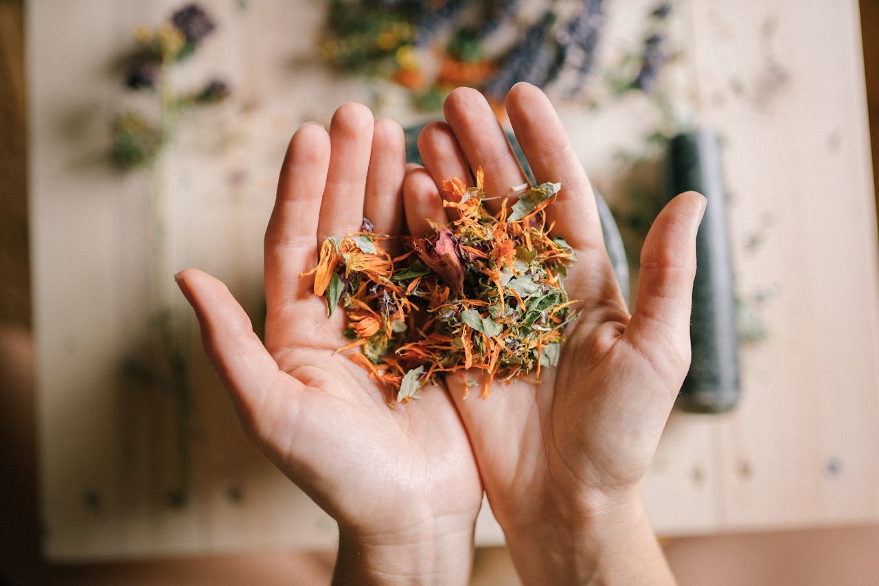 Close-up of hands holding a mix of vibrant dried herbs on a wooden surface.